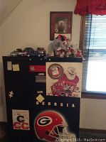 A black filing cabinet decorated with various University of Georgia Bulldogs items including stickers, a small framed picture, and small collectibles on top.