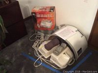 Full view of The Chi Machine, original box in background, cords and manual resting on machine.