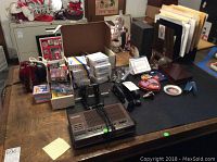 Overall view of assorted office supplies, Elvis memorabilia, electronic devices including old clock radio and stereo, staplers and post-it notes on a wooden table.