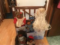 Image showing 7 Raikes brand stuffed bears displayed on wooden railing and floor. Bears have varying outfits and are arranged with 4 original Raikes Bears branded boxes underneath.