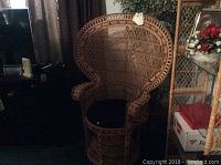 Full view of large wicker chair showing high rounded back, curved armrests, and black cushion on seat.