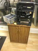 Full view of brown wood media storage cabinet with black plastic shelving unit on top holding various cables and games bin