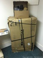 Large Bowflex Revolution branded box strapped closed with plastic strapping, smaller box on top containing seat components