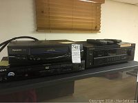Front view of Panasonic VHS player and Pioneer receiver with remotes on top, showing black finish and front control panels