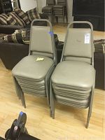 Ten stacked chairs with dark tan vinyl cushions and dark tan metal frames, showing wear and dirt marks