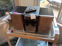 Full view of Sharp stereo system with two speakers and remote control on top, sitting on glass table.