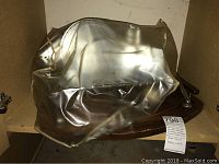 Stainless steel meat slicer covered partly with transparent plastic on a wooden base with side handles.