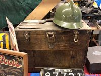 Front view showing vintage wooden toolbox with metal latches and green helmet on top, wood breaking on top panel
