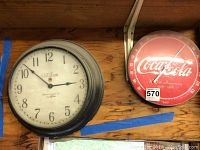 Photo showing both clocks mounted on wood board: the Telechron clock on the left with a white face and black metal casing, and the Coca Cola 100th Anniversary thermometer clock on the right in red with white logo and temperature scale.