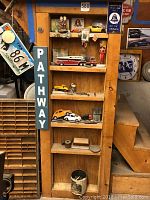 Wooden shelves filled with collectible vehicles and figurines, with vertical "PATHWAY" sign visible on side of shelf.