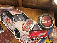 Wide view of Coors Light race car wall decor, Coca-Cola clock, and license plates on wooden wall.
