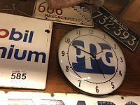 Photo showing PPG round clock mounted on wall, Mobil Premium square sign, and vintage Massachusetts license plates around them.