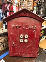 Front view of the red fire alarm box stamped with 'GAMEWELL' and 'FIRE ALARM' featuring four numbered buttons and a lock.