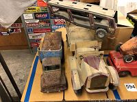 Three vintage metal toy vehicles including 2 rusted automobiles and a military cargo truck model positioned together on a table with a background of signage.