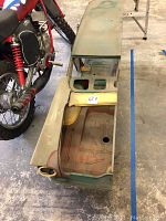 Top view of primered car body shell showing floor pan, roof openings and wood support base