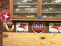 Overview of five metal signs mounted on wood wall beneath display cabinet