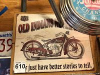 Close-up of Old Indians metal sign featuring a red vintage motorcycle and slogan on an aged white background.