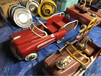 Front left perspective showing red station wagon pedal car with white steering wheel and wheels, green and white side decals, silver grille