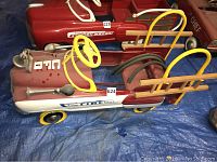 Side view of red and white pedal car labeled 624, showing steering wheel, front grille shape, yellow wheels, side ladder rack and coiled hoses