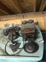 Wooden ringer box with dual bells, side crank and cord attachments atop blue surface