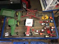 Wide shot of lot showing two green John Deere toy tractors with attached carts, a red farming implement, and around 15 smaller model trucks and tractors in different colors grouped together.