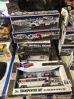 Multiple boxed model trucks including Hess utility tow trucks, Tonka rescue vehicle, Richard Petty 3-piece transporter with stock cars, and 1993 Indianapolis 500 die-cast truck bank
