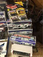 Photo showing collection of boxed Hess trucks and NASCAR car set and partially visible boxed Dodge Daytona model.