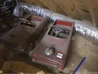 Overview of two red metal pedal cars on attic floor