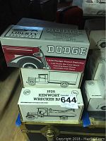 Boxes of vintage collectible die cast model vehicle banks stacked on table including Dodge, Kenworth, and more.