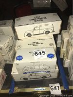 Seven boxed collectible model bank trucks arranged on floor and cart, showing box labeling and artwork.