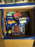 Box filled with various unopened Hot Wheels toy car packages showing different colors and car models inside a cardboard box.