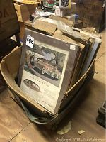 Photo of box containing assorted vintage car prints labeled Chevrolet, Cadillac, Packard