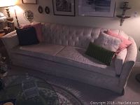 Full view of couch showing light beige color with tufted backrest and various pillows arranged on it.