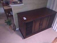 Photo of the large dark wooden stereo cabinet from front angle showing slatted doors and solid top