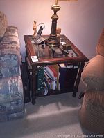 Full view of the wooden side table with glass top placed between sofa and chair, showing some items on the lower shelf.