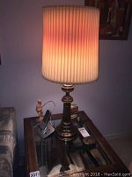 Photo showing the vintage table lamp with pleated shade and decorative base, lit inside to show warm glow