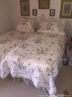 Two twin beds with white metal headboard and floral bedding arranged side by side against wall decorated with framed artwork.