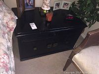 Black wooden side table shown from front with cabinet doors and items on top.