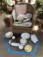 Overall view of assorted kitchen bowls, trays, crocks, and baking dishes arranged on a wicker chair and floor space.