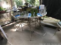 White metal round patio table with various items on top, showing rust spots and wear on the legs and frame.
