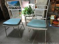 Four white metal outdoor patio chairs with blue vinyl cushions, showing some peeling paint and rust