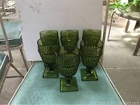 Eight green glass goblets with textured pattern arranged on a blue surface.