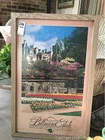 Large framed poster of Biltmore Estate with garden in foreground and blue sky background. The frame is approximately 2 inches wide with a natural wood finish.