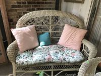 Full front view of the white painted wicker bench with the floral cushion and three pillows.