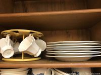 Shelf with stacked plates, bowls, and mugs on rotating rack showing mug handles and plate edges.