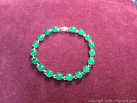 Photo of a woman's bracelet featuring round green jade stones set in gold-tone metal on a red velvet surface.