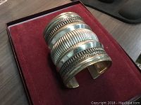 One photo of a large woman's bangle bracelet resting on a red velvet surface showing the band design details.