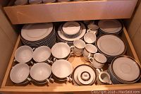 Drawer containing stacked dinner plates, bowls, saucers, and teacups