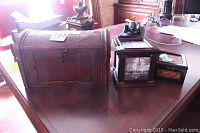 Medium curved wooden hinged box with metal latch, showing front and side, on wooden table along with other decor items.