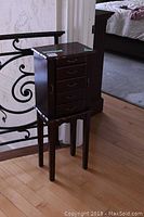 Full view of the dark wood jewelry cabinet showing front with five drawers and legs